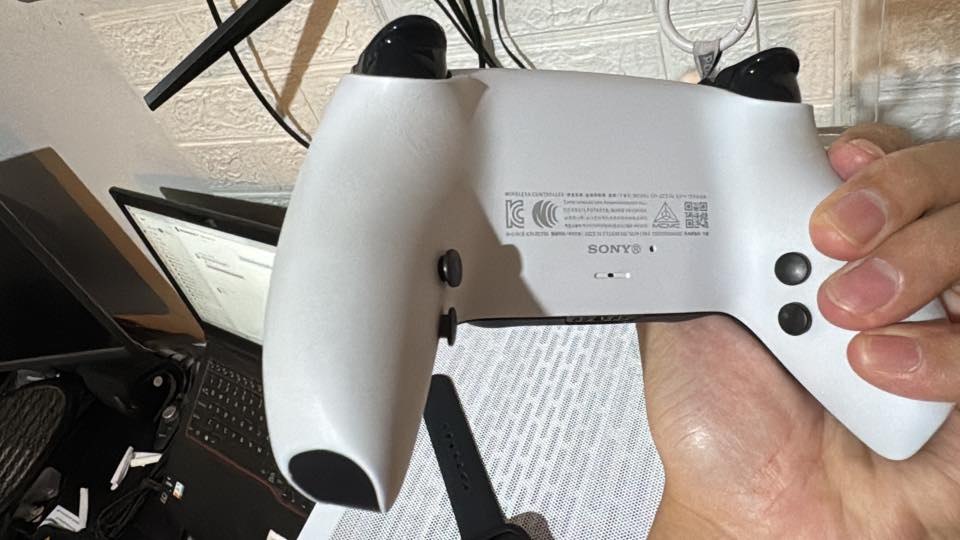 Rear view of a white customer DualSense controller with four black buttons